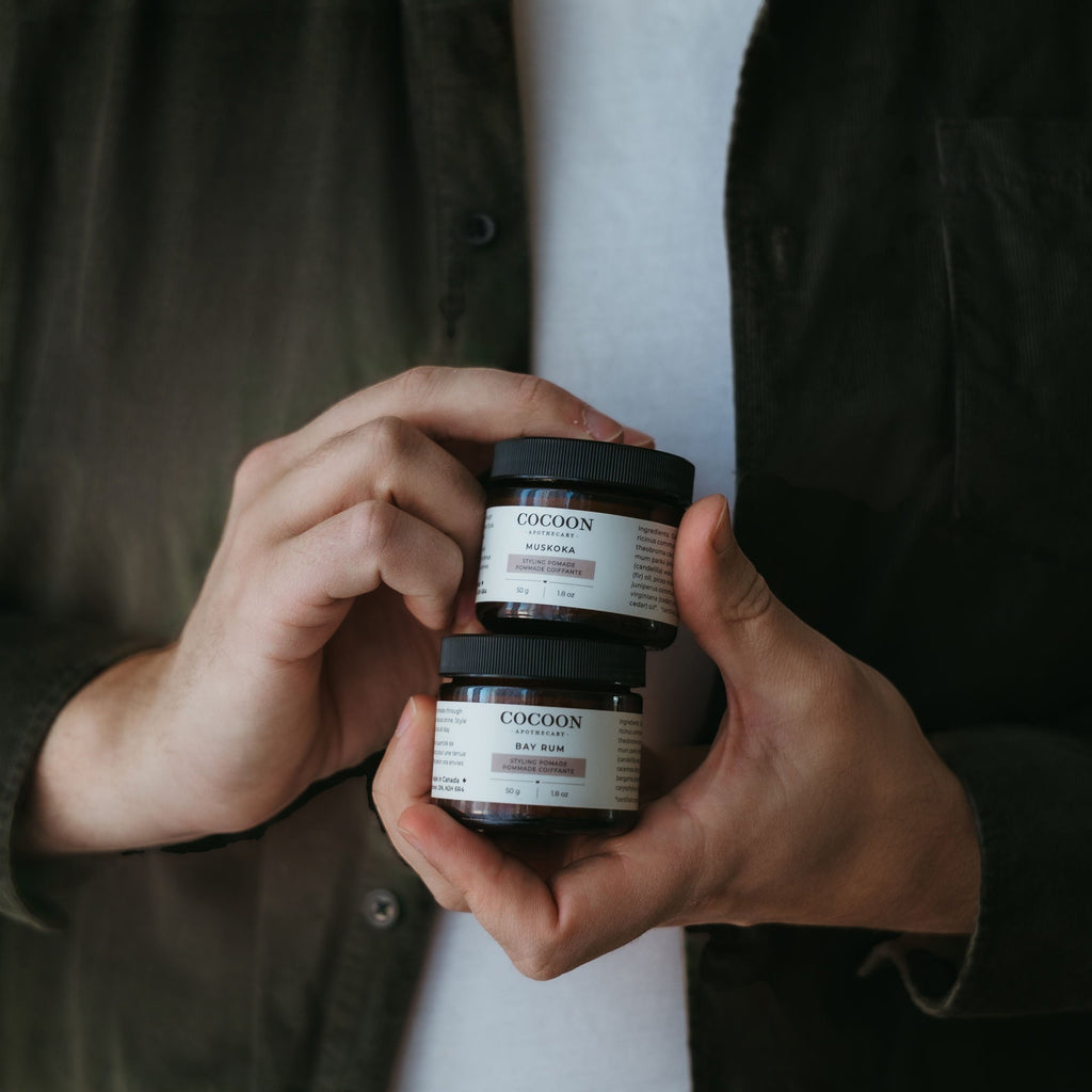 Oh Canada Gifts Muskoka and Bay Rum styling pomade jars held in hands by a person wearing a dark green shirt