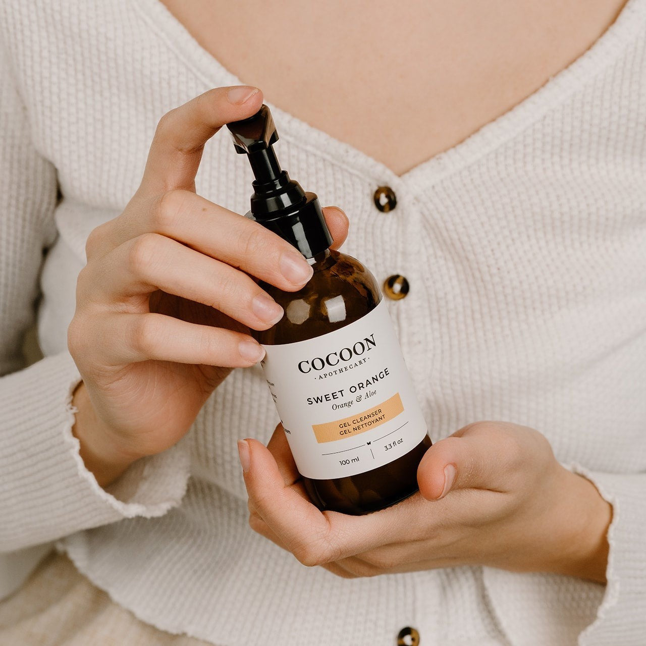Oh Canada Gifts Cocoon Apothecary Sweet Orange Gel Cleanser in a brown pump bottle held by a woman in a white top.