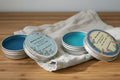 Oh Canada Gifts grass-fed tallow balm tins in blue, featuring botanical labels on a linen cloth on a wooden surface.