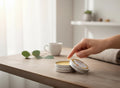 Oh Canada Gifts Root & Sky throat and neck salve in a small metal tin with a hand applying the balm on a wooden table