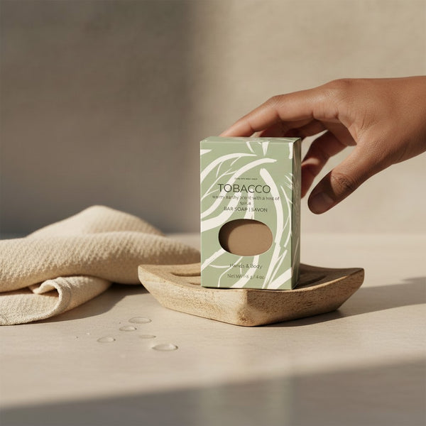 Oh Canada Gifts tobacco leaf soap bar in a green box on a wooden soap dish with a beige cloth in a minimalist setting.