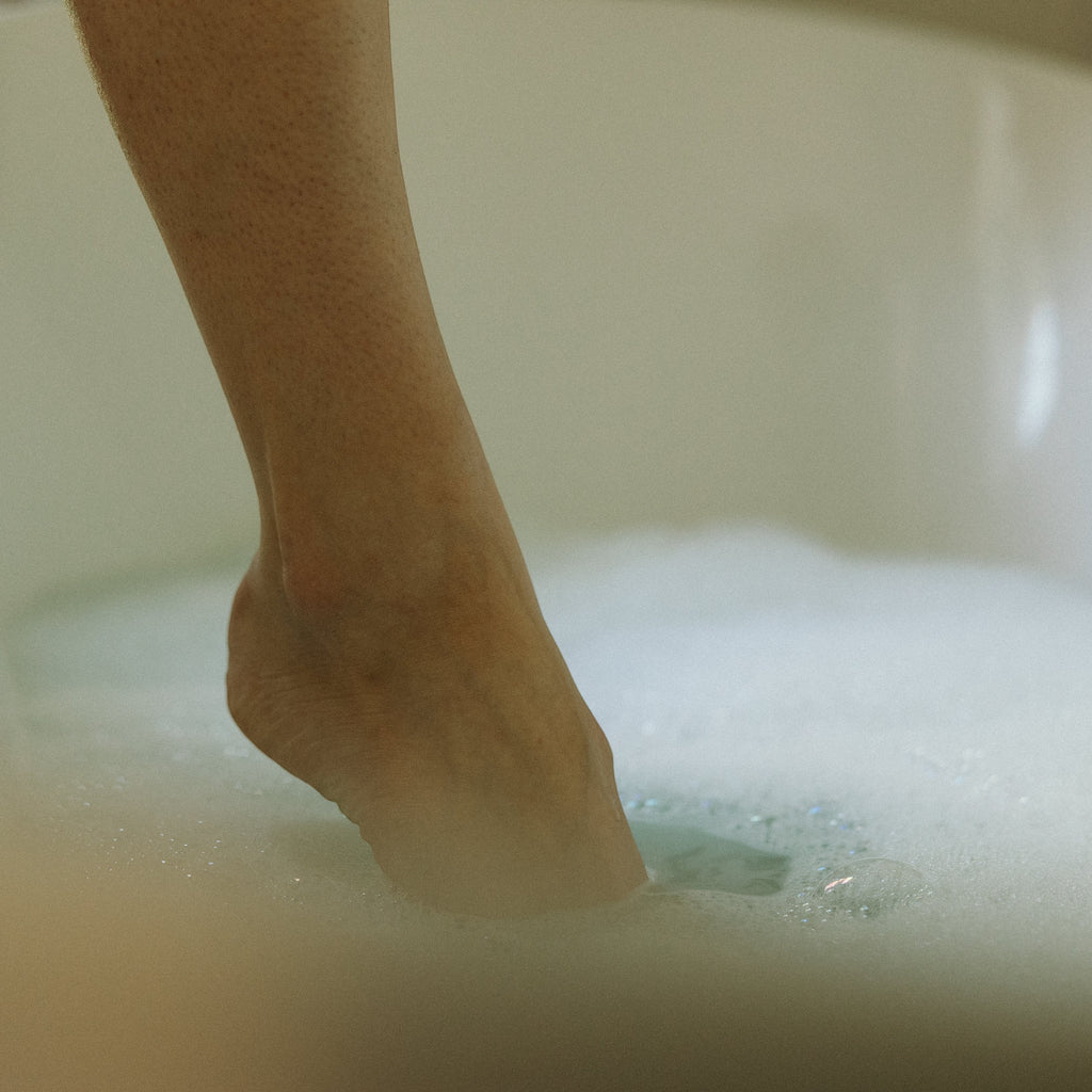Oh Canada Gifts Touchy Feely bubble bath with lavender and rosemary, showing a foot soaking in rich, delicate bubbles.