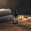 Oh Canada Gifts Ubermint beard oil in an amber glass pump bottle on a wooden surface with a towel and wooden comb.
