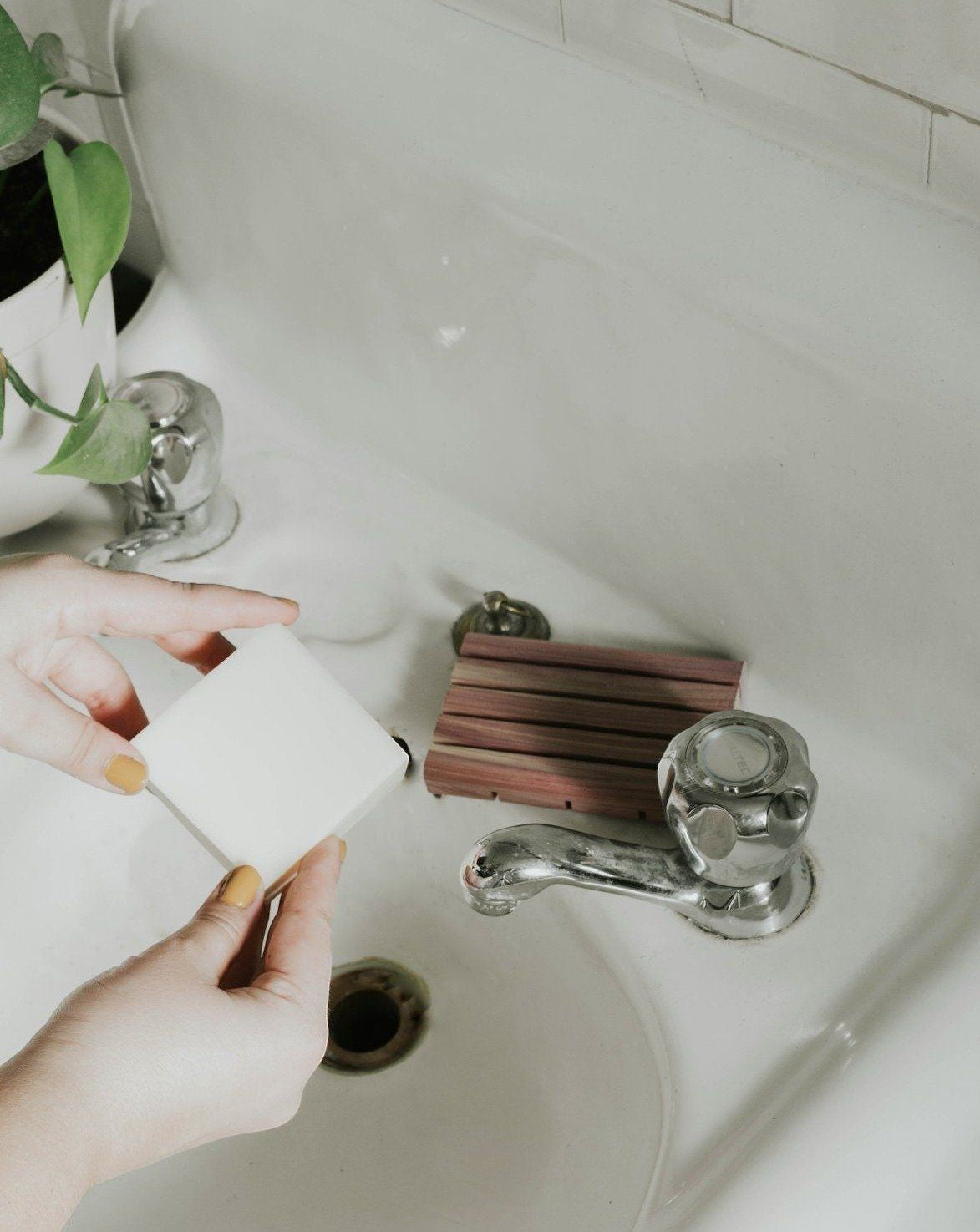 Oh Canada Gifts unscented solid dish soap bar held over a white kitchen sink with a wooden cedar soap tray