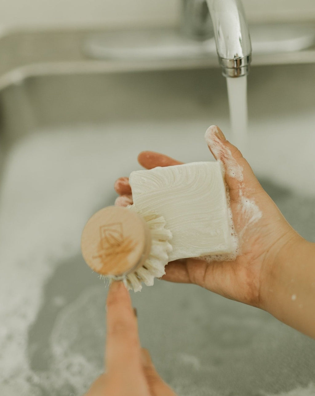 Oh Canada Gifts unscented solid dish soap bar being lathered with a wooden dish brush over a kitchen sink