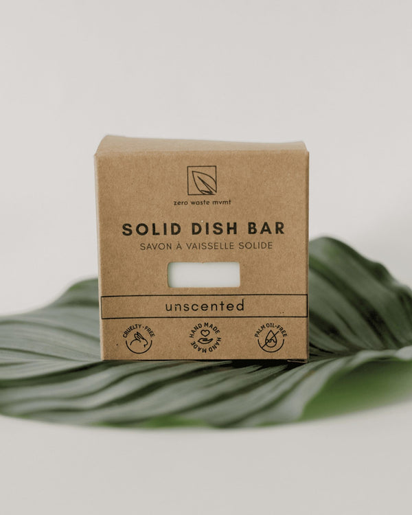 Oh Canada Gifts unscented solid dish soap bar in eco-friendly cardboard packaging resting on a green tropical leaf.