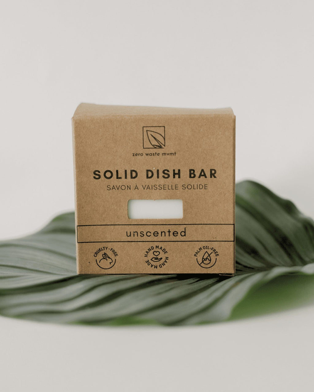 Oh Canada Gifts unscented solid dish soap bar in eco-friendly cardboard packaging resting on a green tropical leaf.