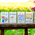 Oh Canada Gifts wildflower seed packages with colorful floral designs and messages on a rustic wooden bench.