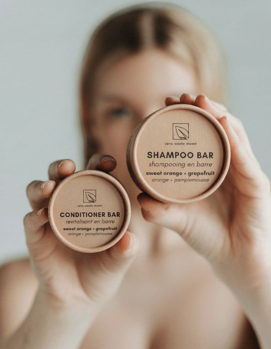 Oh Canada Gifts zero-waste shampoo and conditioner bars in sustainable cardboard packaging held by a woman.